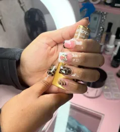 Hands with gold and patterned long nails being held up in a pink nail salon.