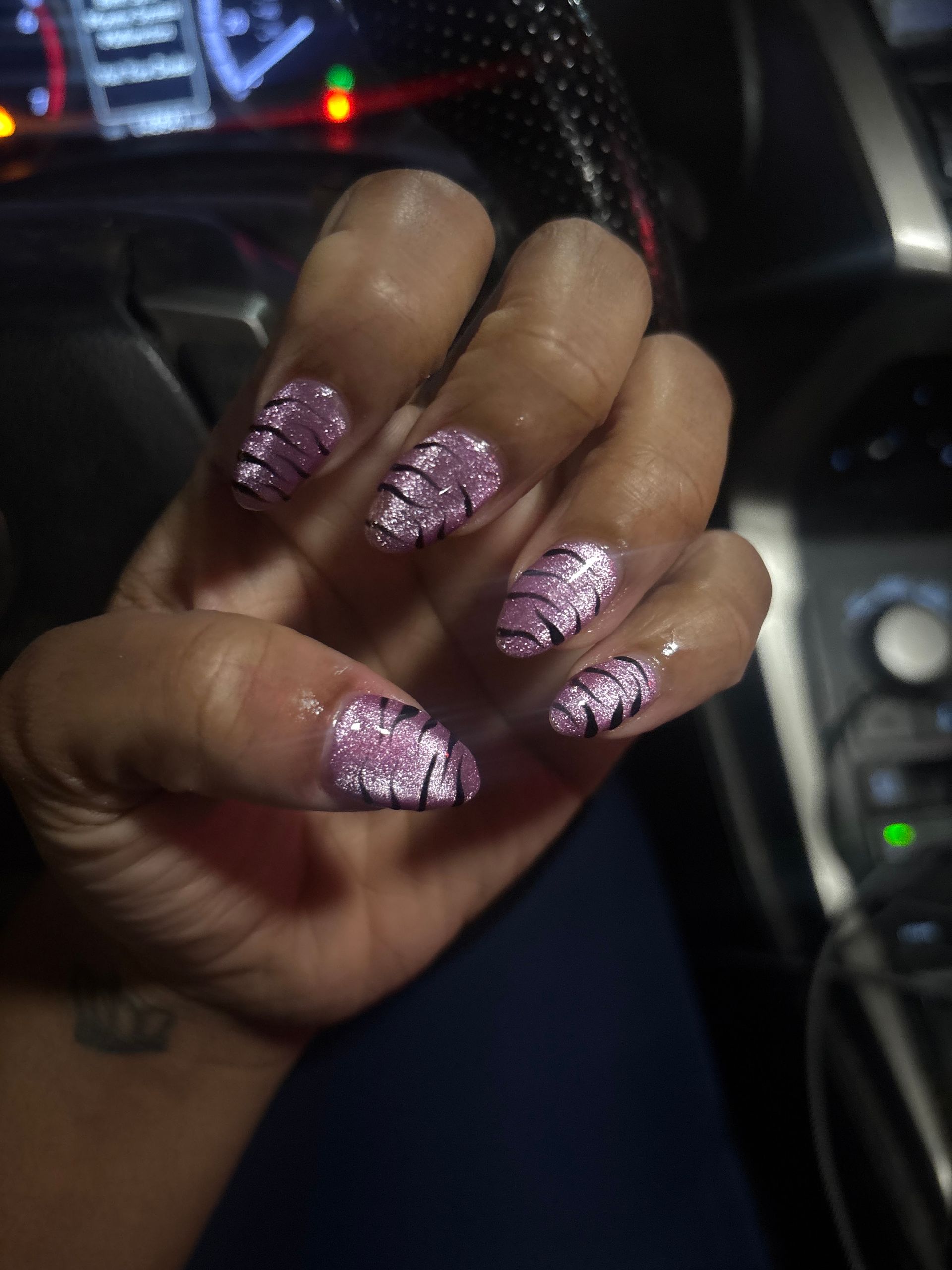 Hand with pink glitter manicured nails inside a car at night