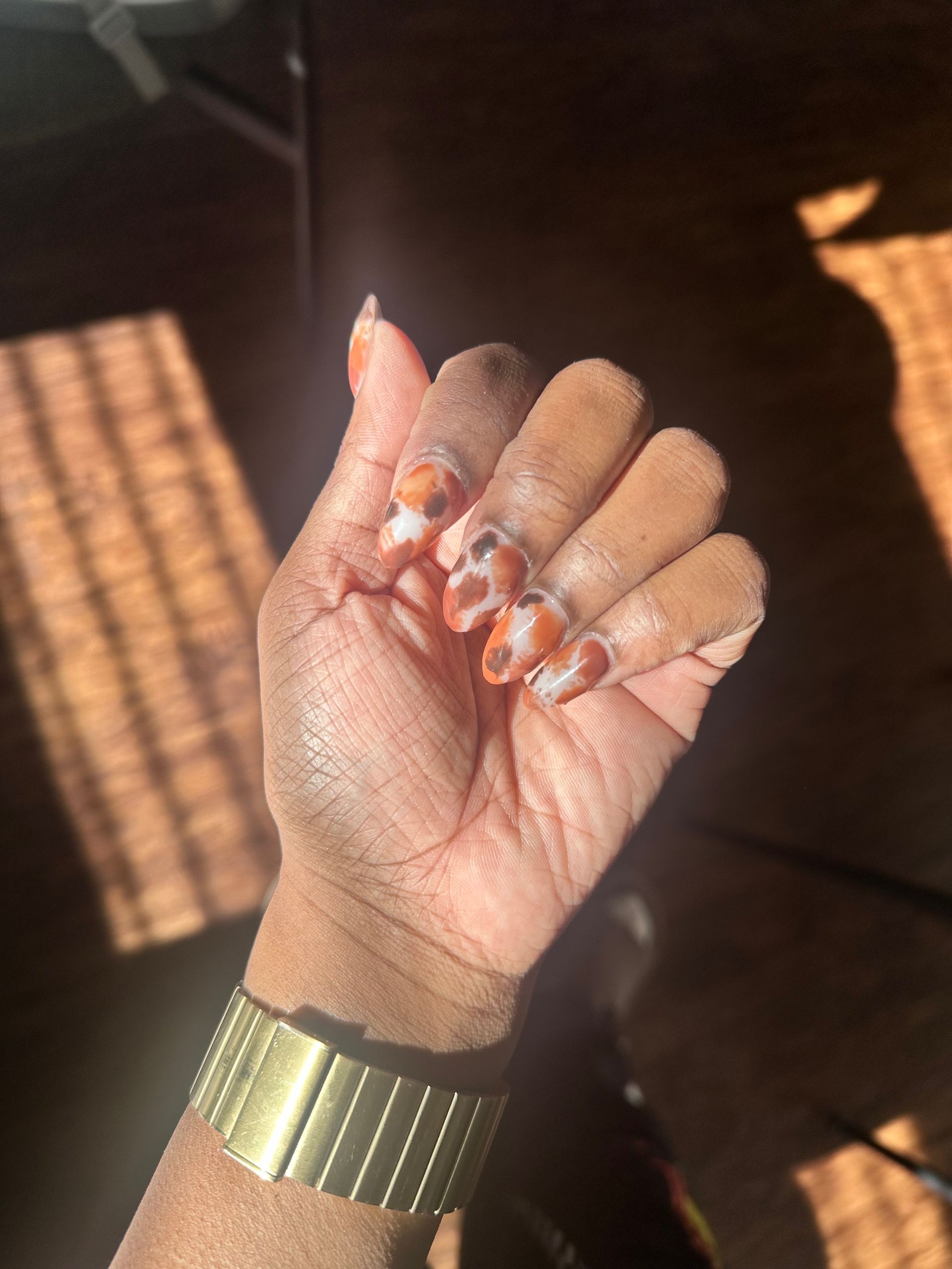 Hand with orange-tipped nails and a green watch in warm sunlight.