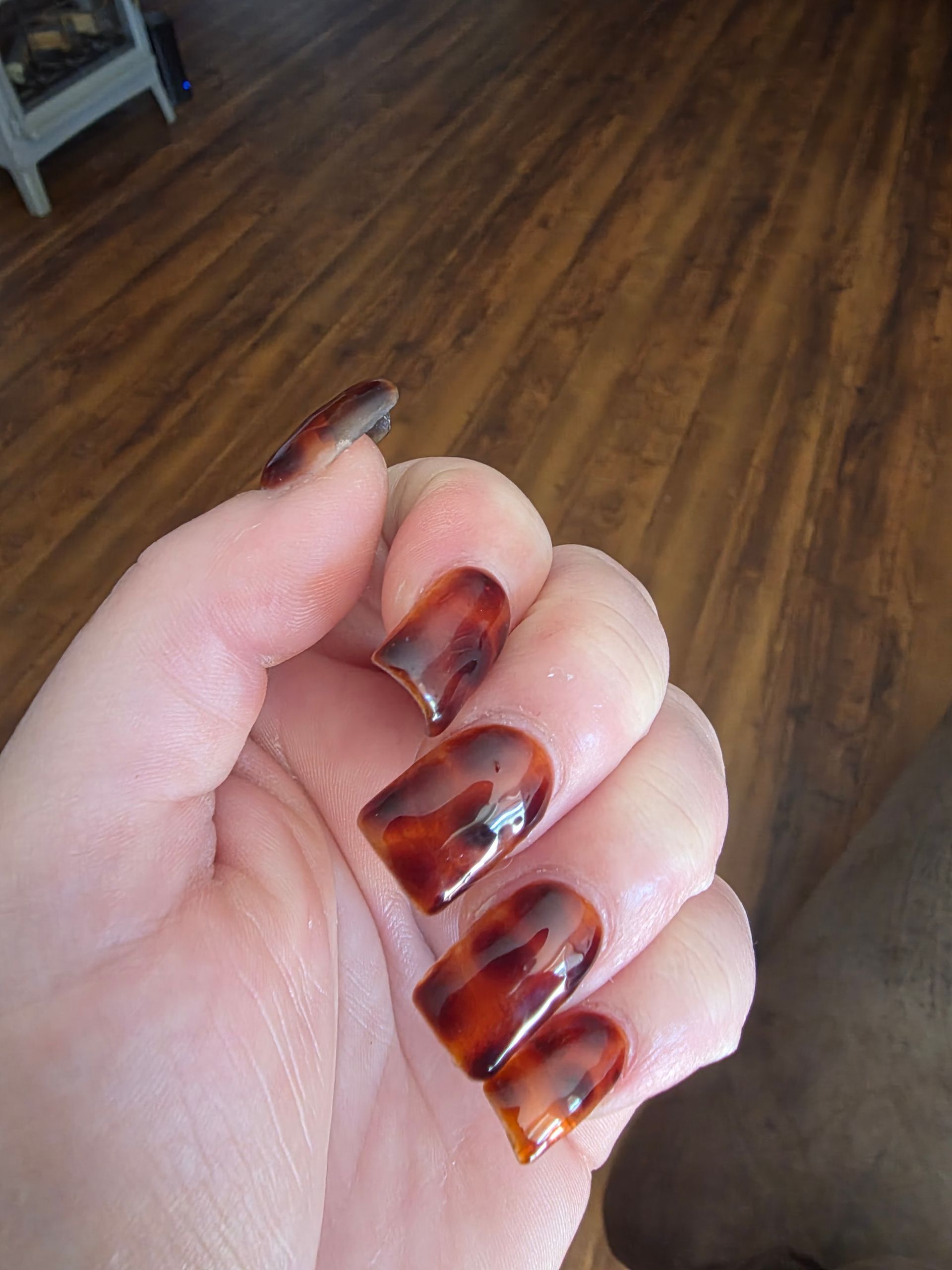Hand with long brown tortoiseshell acrylic nails against a wooden floor