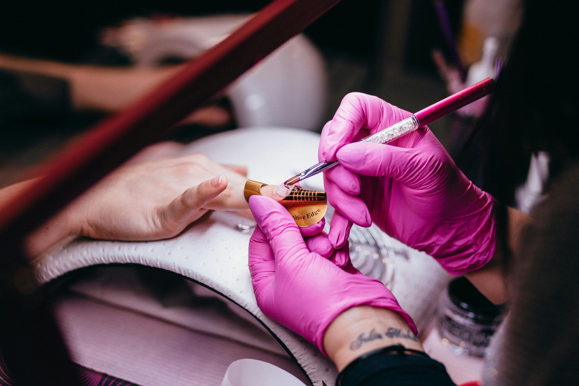 Gloved hands applying nail polish to a fingernail in a salon