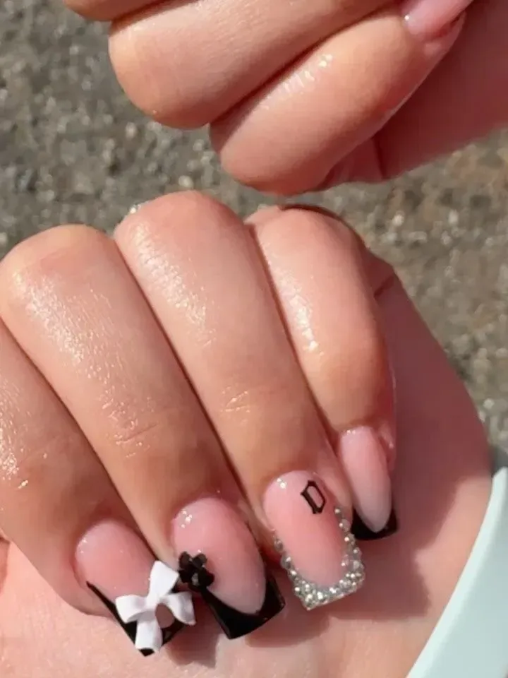 Close-up of manicured pink nails with black and white bow accents and silver glitter detail