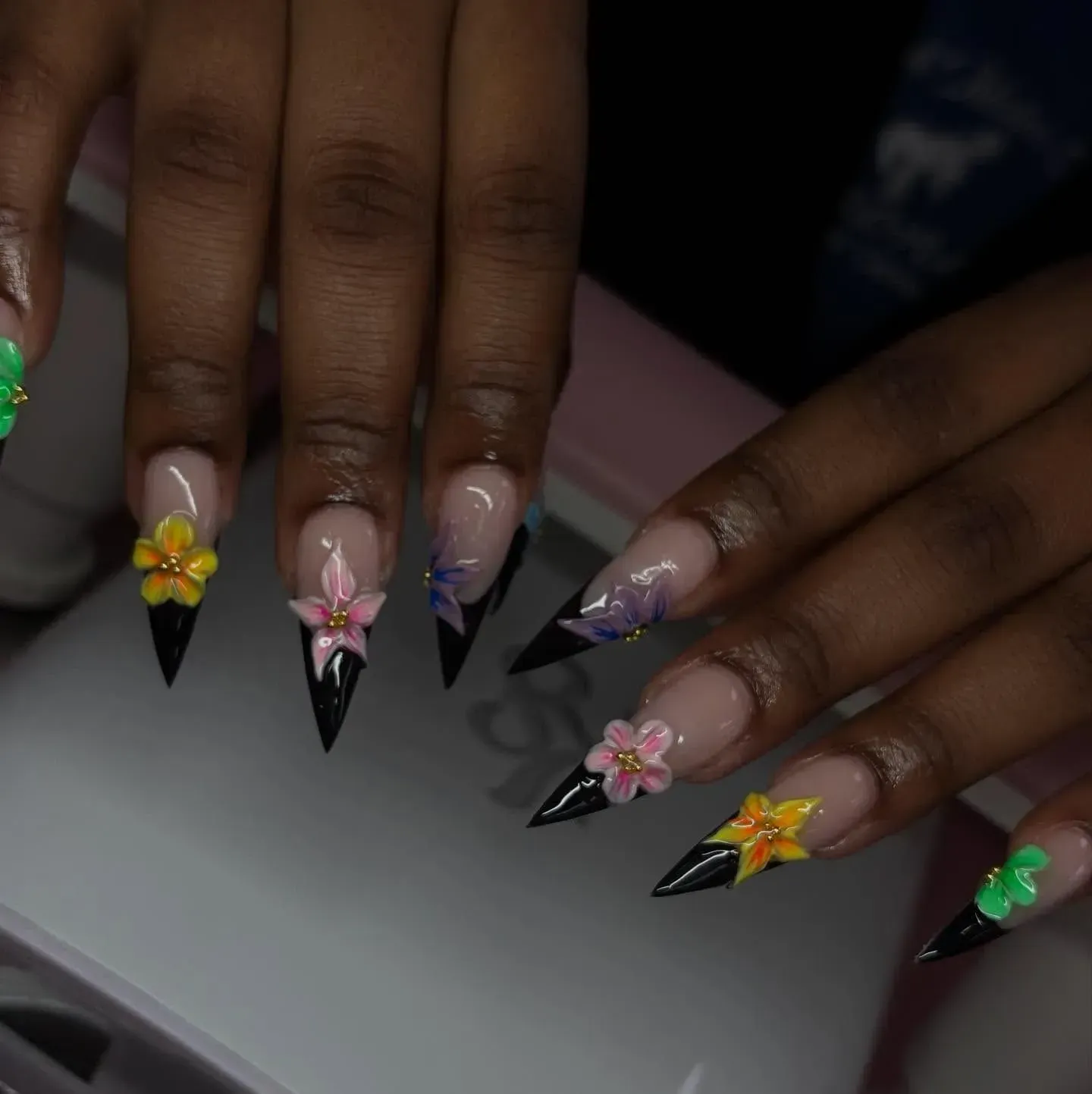 Hands with long black stiletto nails, decorated with colorful floral nail art.