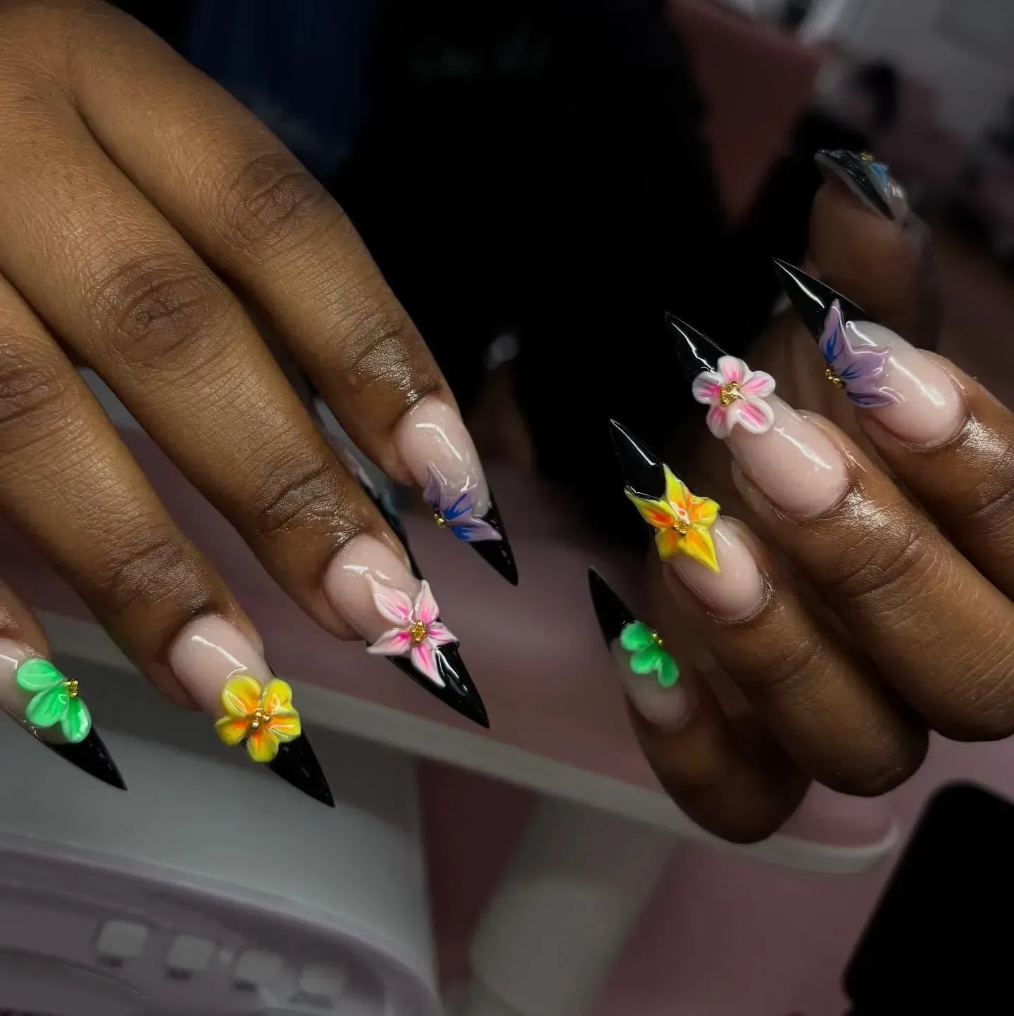 Hands with long pastel floral acrylic nails and black pointed tips on a soft pink background