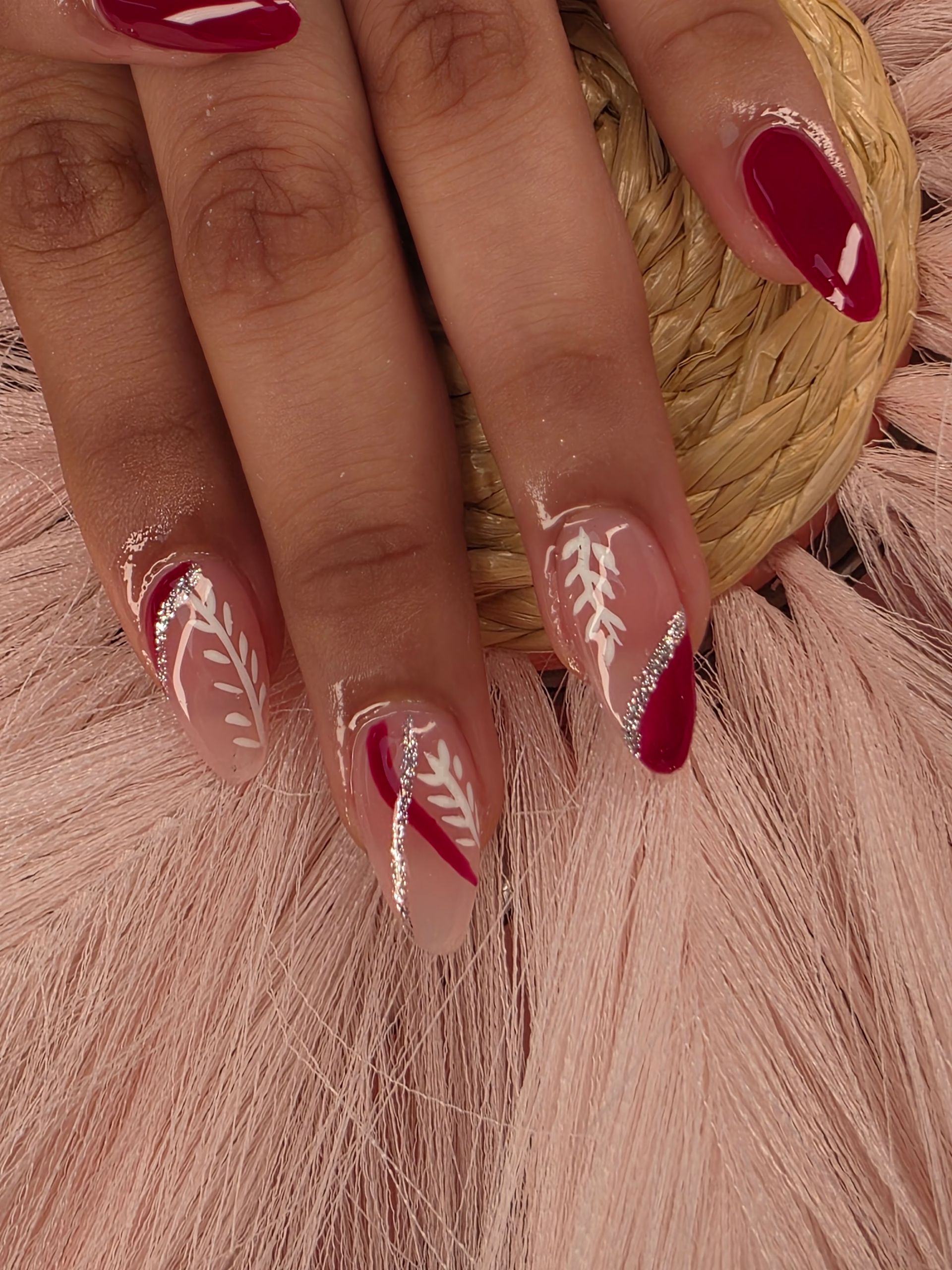 Hand with long red and clear nail art resting on pink fabric and a woven straw surface
