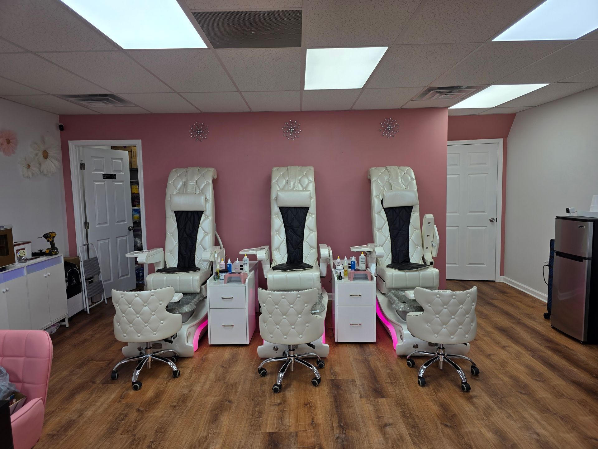 Pink nail salon with three pedicure chairs and foot spas under bright ceiling lights