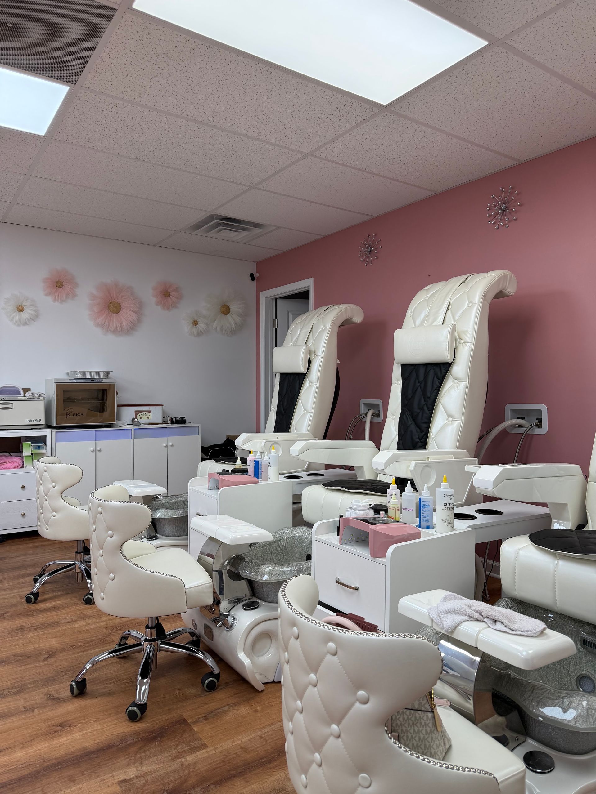 Pink nail salon with pedicure chairs, manicure stations, and bright ceiling lights
