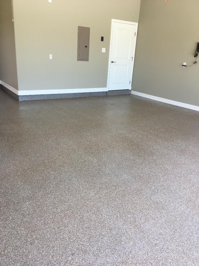 Empty beige room with speckled floor, white baseboards, and electrical panels on the wall