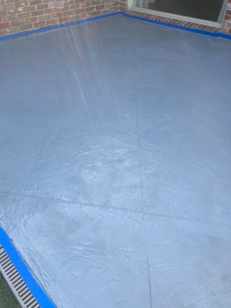 Empty blue-gray concrete floor in a brick-walled corner, with a drain along the edge.