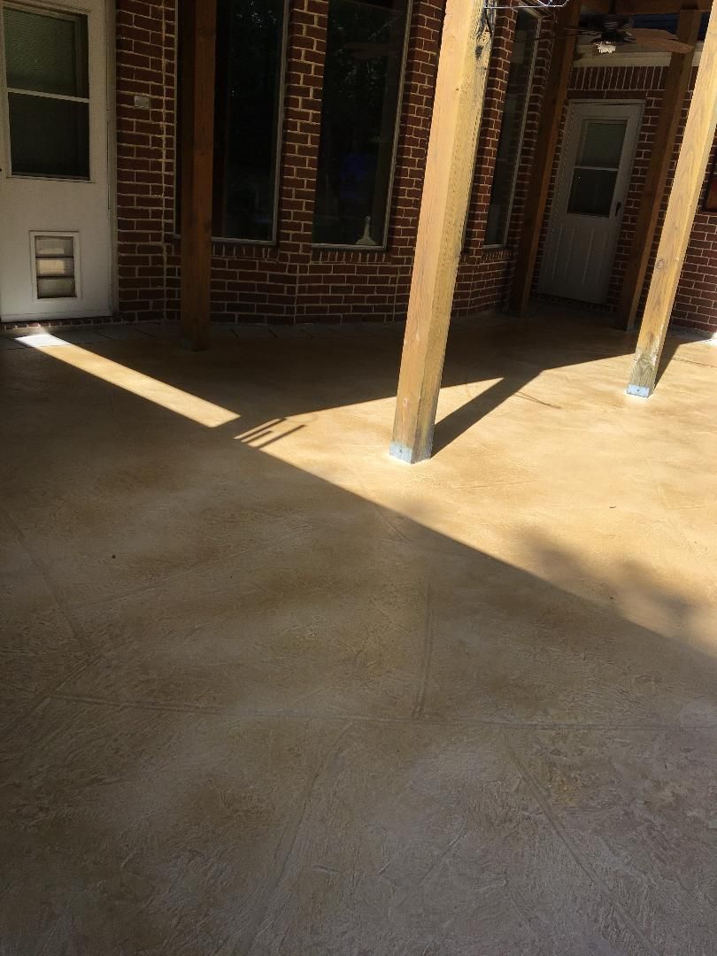 Covered brick courtyard with concrete floor, wooden support posts, and strong sunlight casting shadows