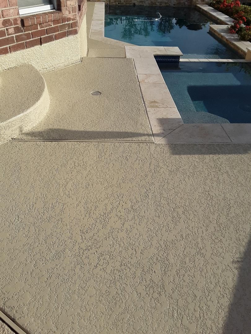 Backyard patio with textured concrete beside a swimming pool and spa, bordered by brick and stone trim