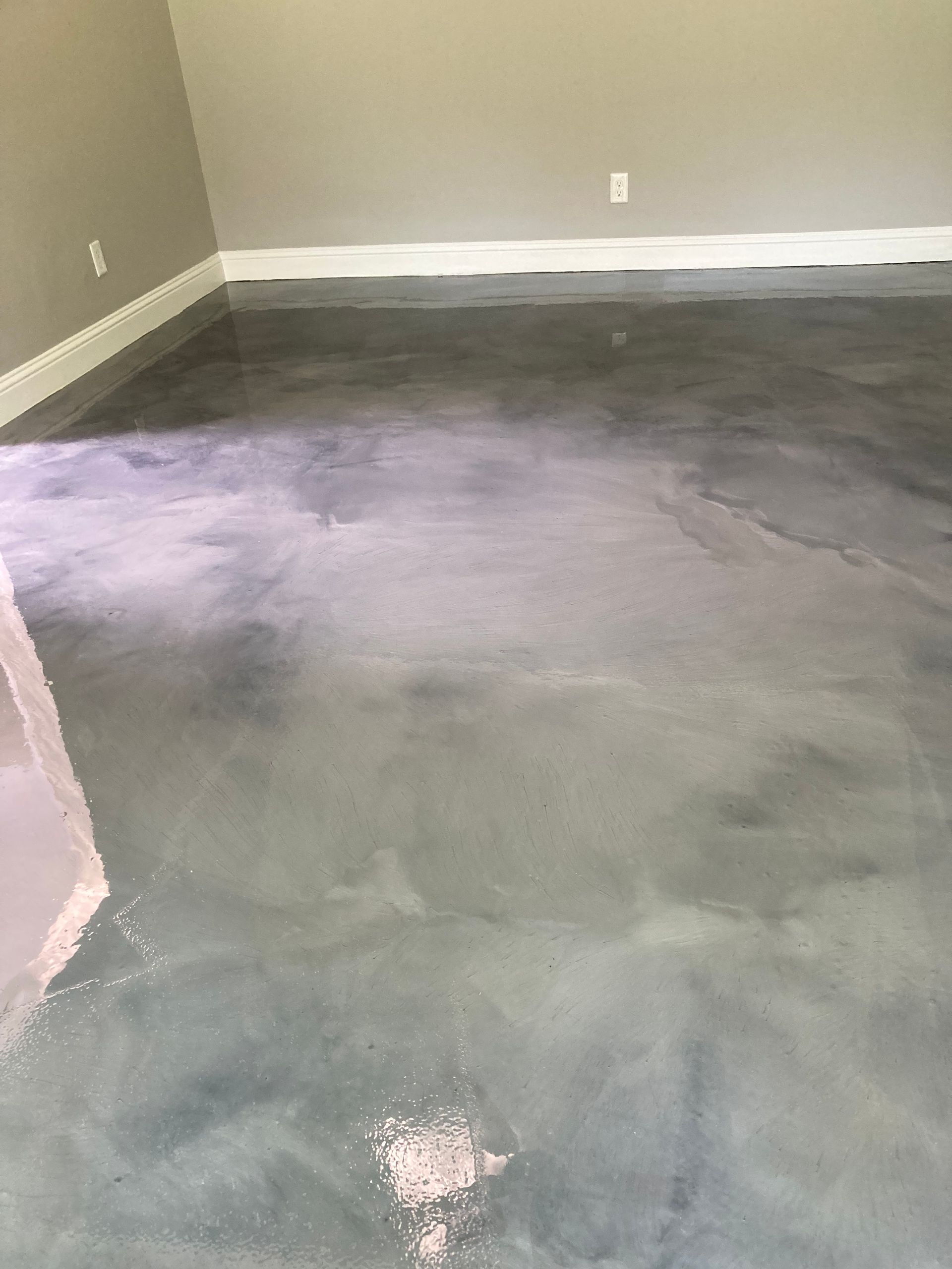 Empty room with a gray concrete floor and beige walls, showing a large wet patch near the center.