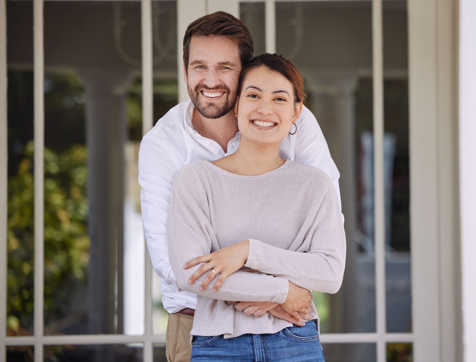 Smiling couple embracing in front of a house with white shutters