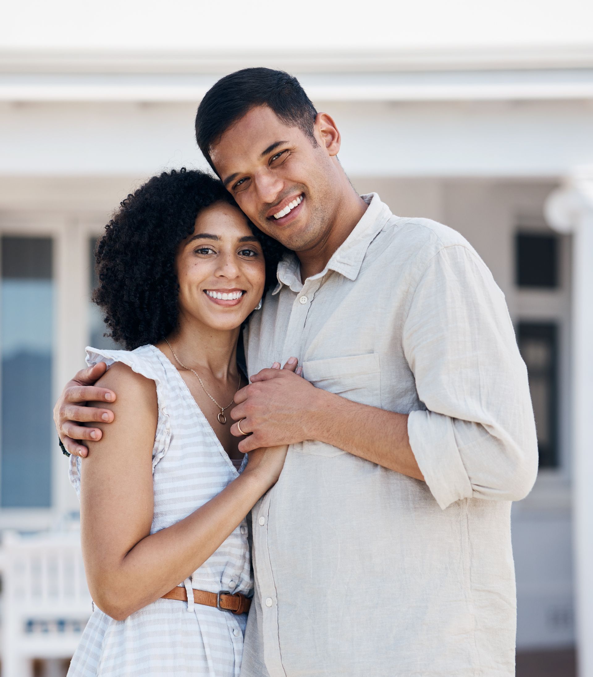 Two smiling people hugging outdoors in front of a white building
