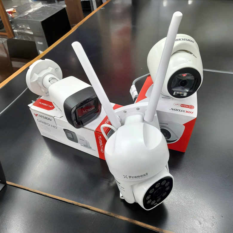Tres cámaras de seguridad inalámbricas blancas con antenas, colocadas en cajas sobre una mesa negra.