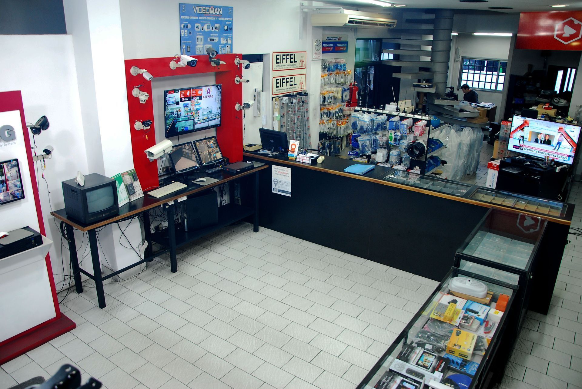 Mostrador de caja de una tienda de conveniencia con bocadillos, bebidas y un televisor al fondo.
