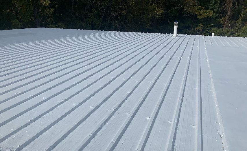 A flat coated corrugated metal roof with a vent pipe.