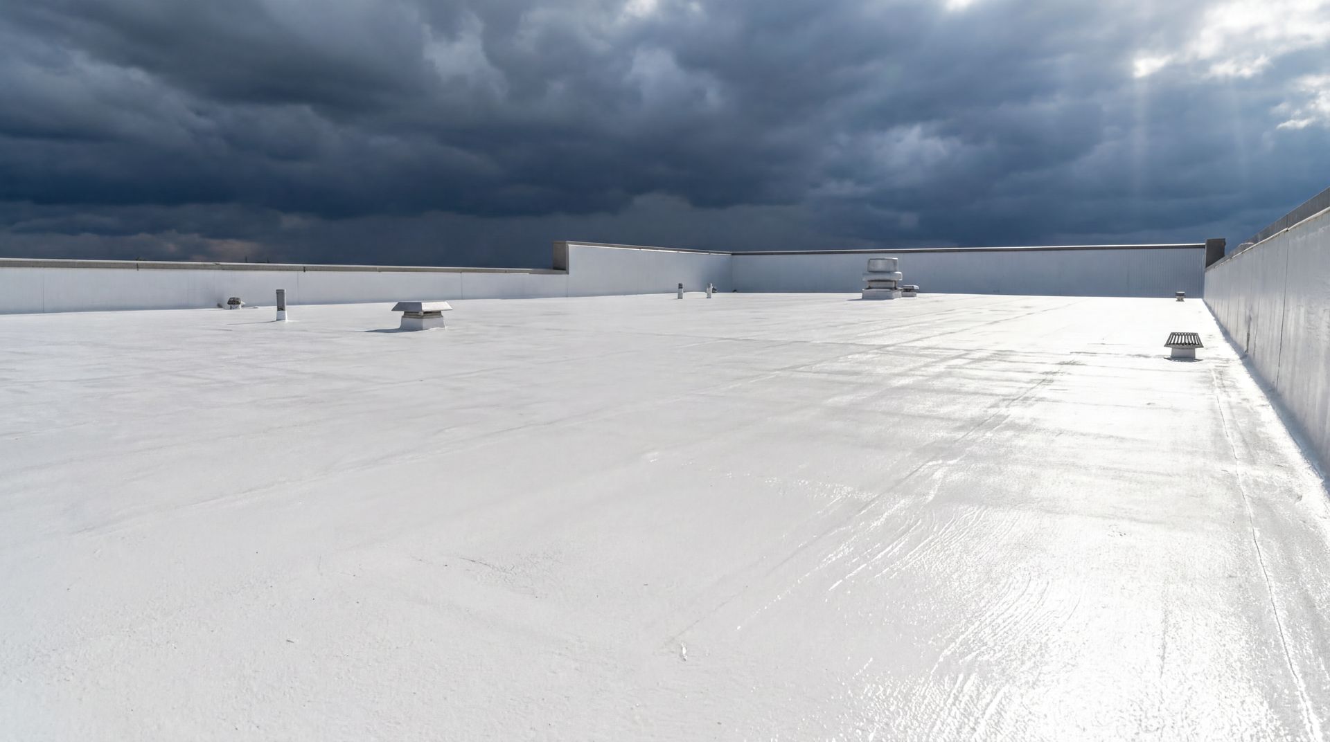 White roof coating on a commercial low-slope roofing system beneath approaching storm clouds.