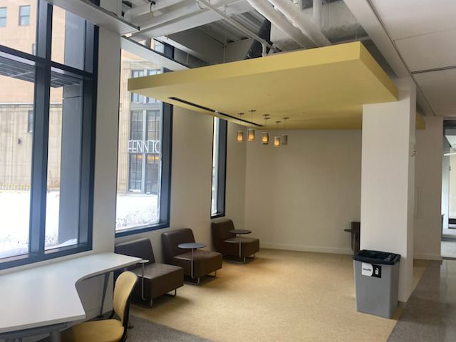 Modern office lounge with chairs, desk, large windows, and a yellow ceiling panel