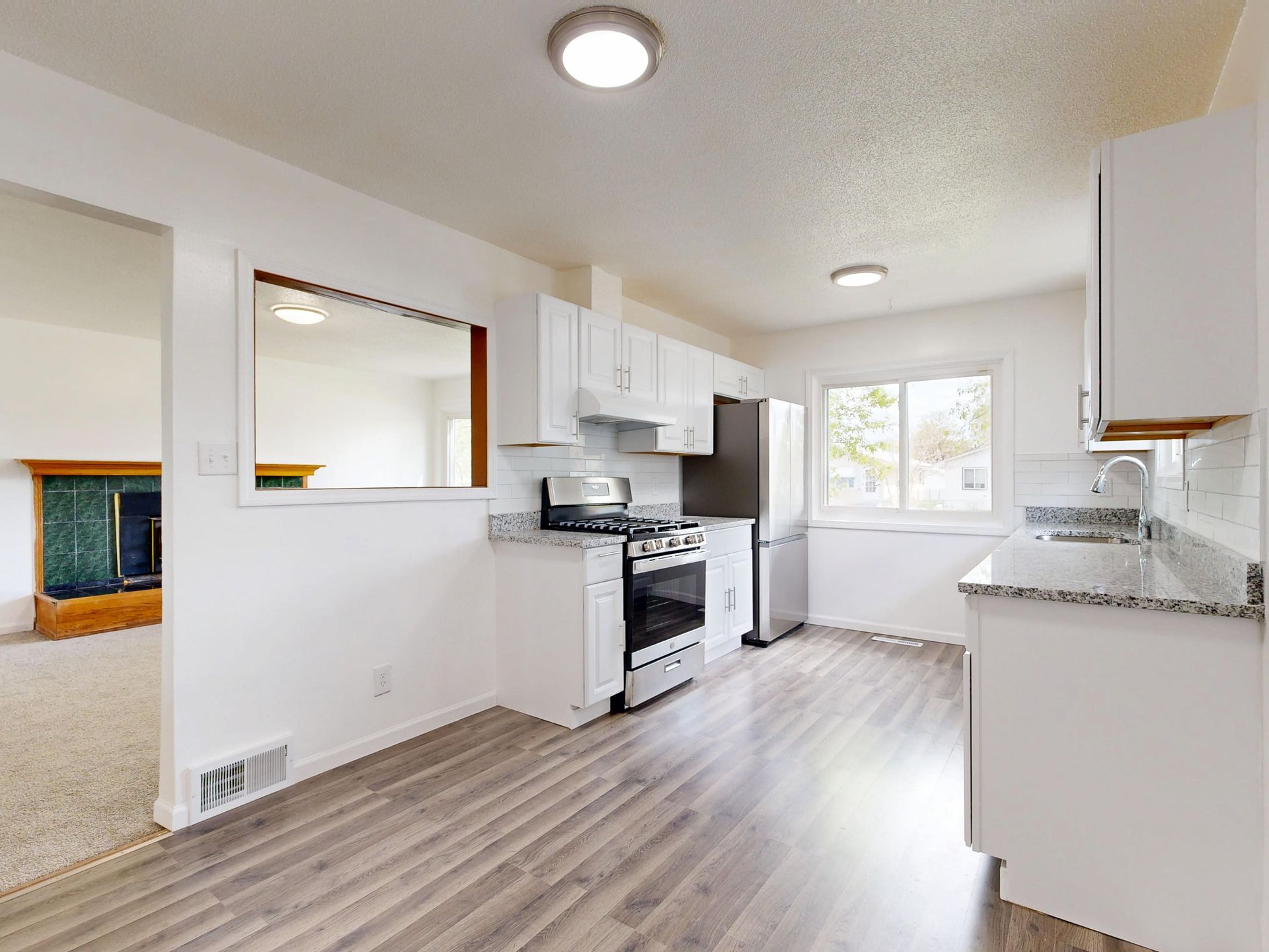 Bright white kitchen with stove, cabinets, gray countertops, wood-look floor, and a windowed dining nook