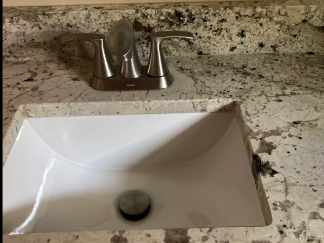 White bathroom sink with chrome faucet on speckled granite countertop.