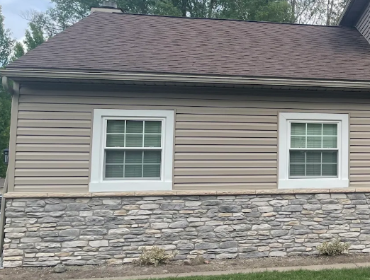 Single-story beige house with white-trim windows and a stone veneer lower exterior under a brown shingled roof