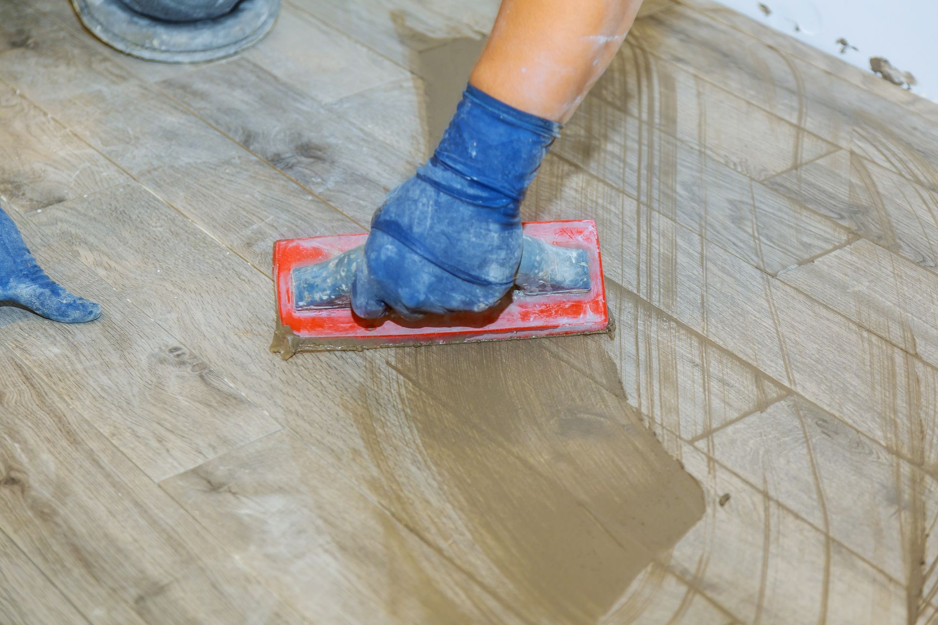 A person is using a trowel to spread cement on a tile floor.