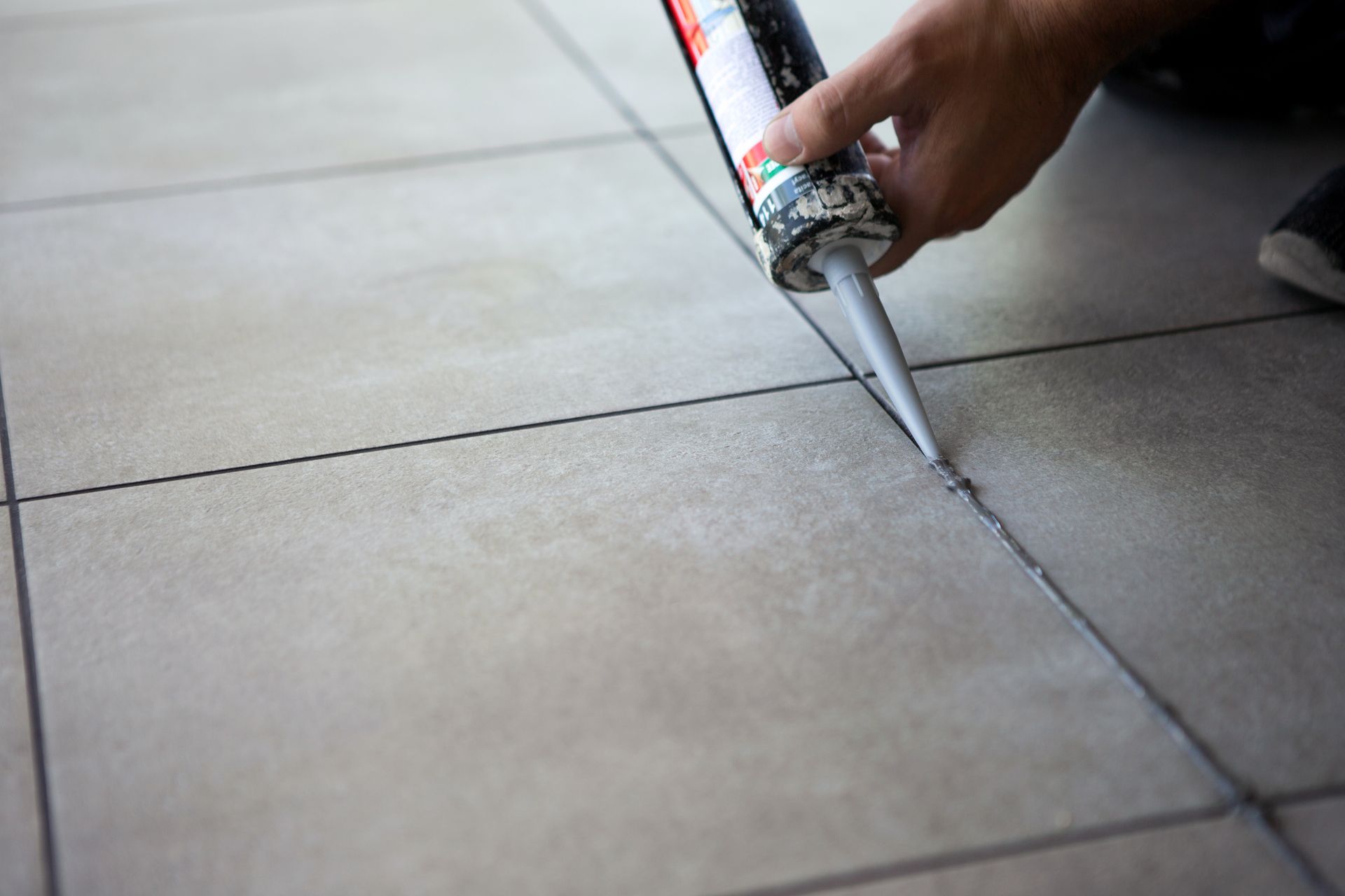 A person is applying sealant to a tile floor.