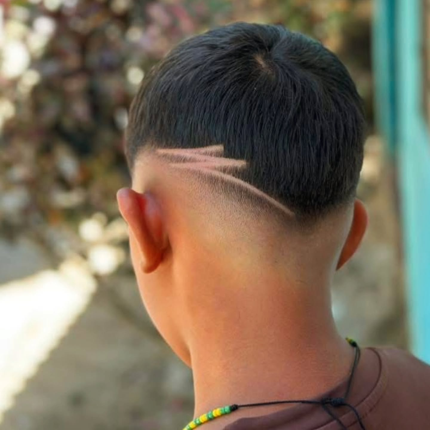 Back of a person with a short fade haircut and shaved design, outdoors