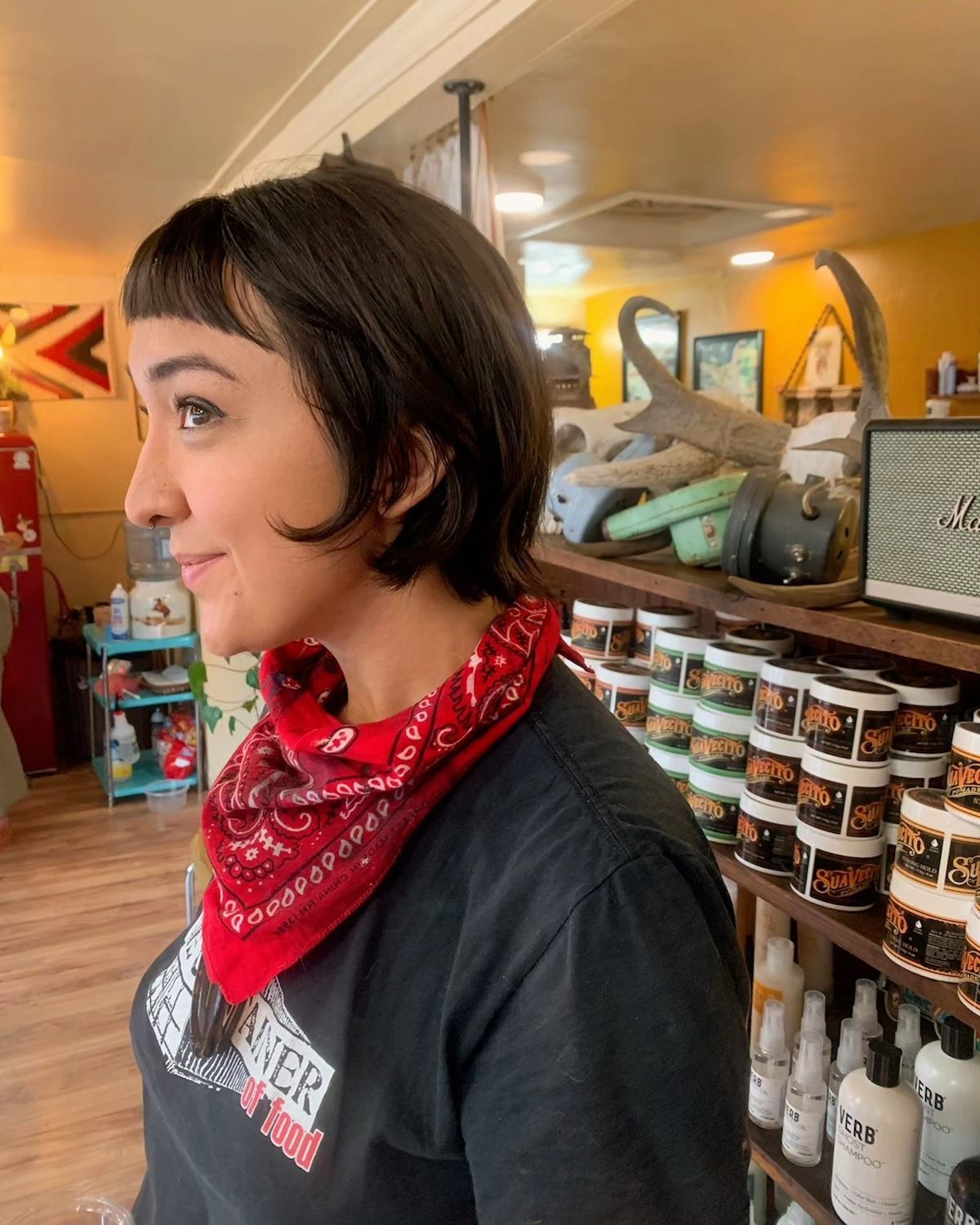Person in a red bandana stands in a shop with shelves of jars and bottles in the background.