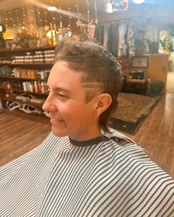 Person smiling in a barber shop, wearing a striped cape with a short haircut.