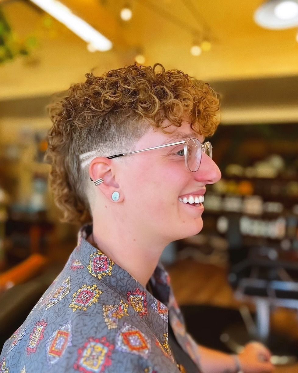 Profile of a smiling person with curly hair and glasses in a warm, softly lit cafe