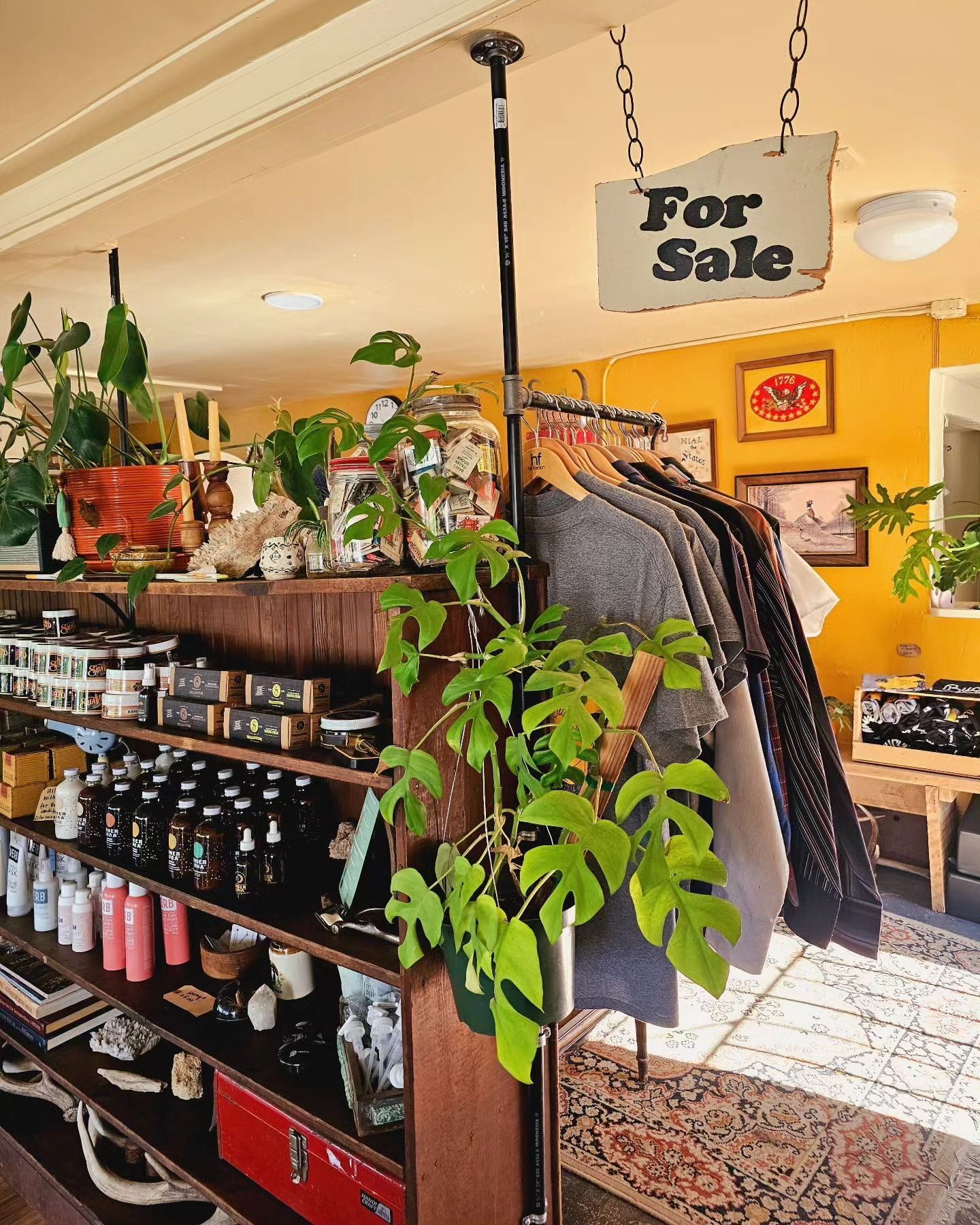 Clothing store interior with racks, shelves of products, and a hanging “For Sale” sign