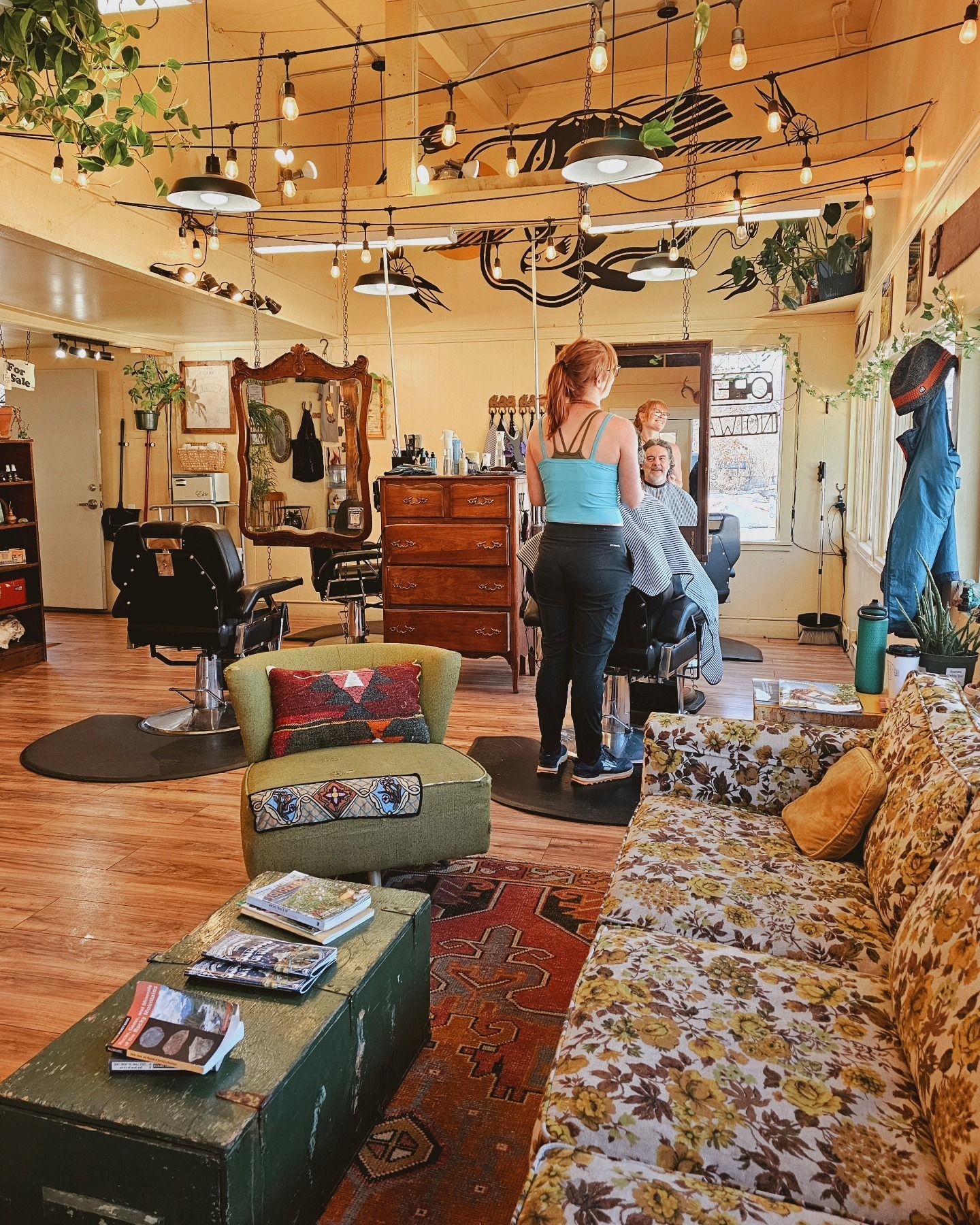 Cozy vintage shop interior with hanging lights, rugs, furniture, and two people browsing.