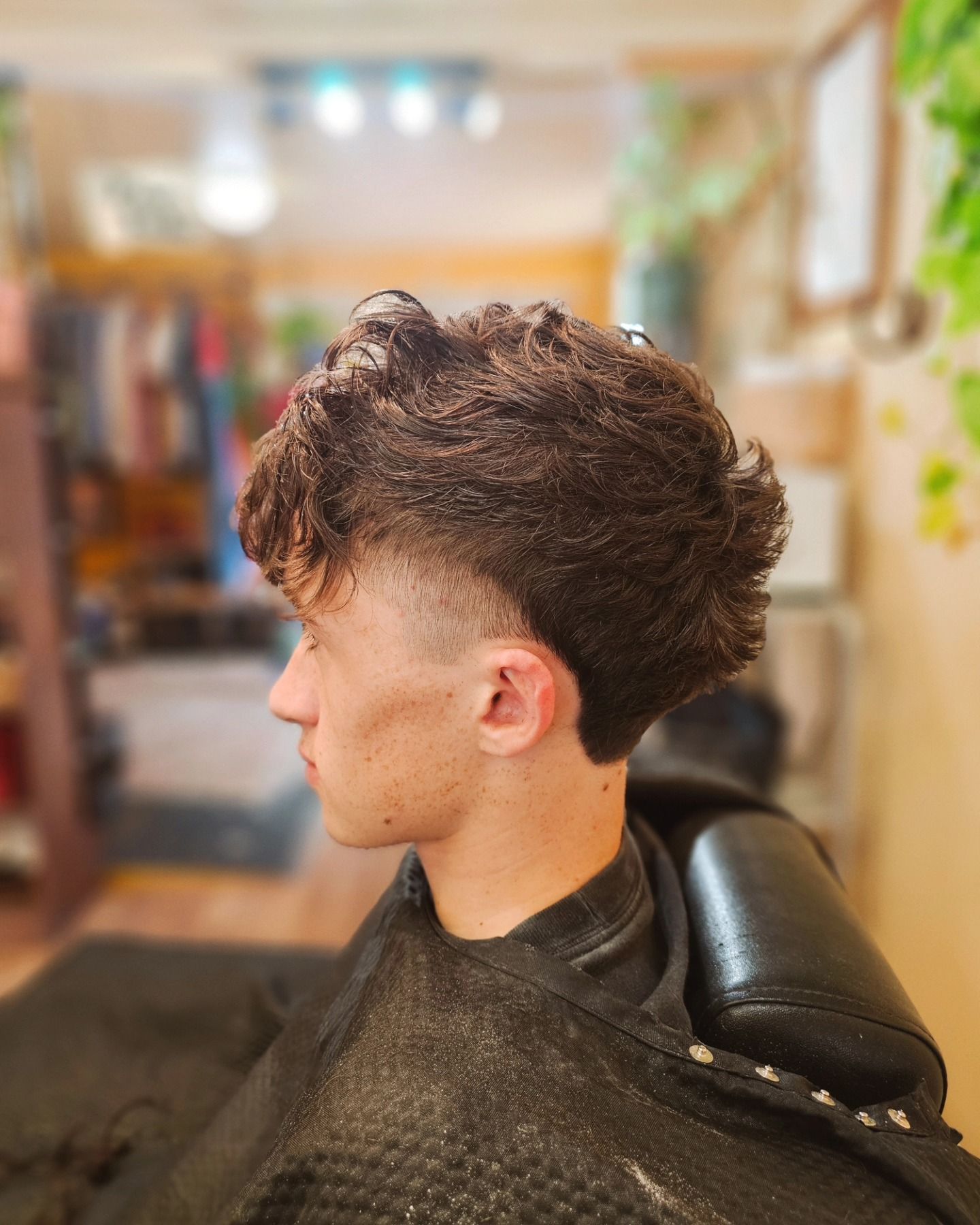 Side profile of a person with a textured curly haircut in a salon chair, wearing a black cape.