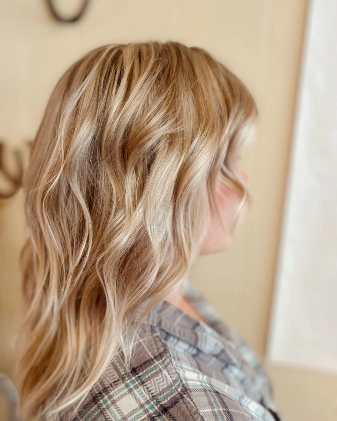 Side view of wavy blonde hair with subtle highlights, worn over a plaid shirt in warm indoor light