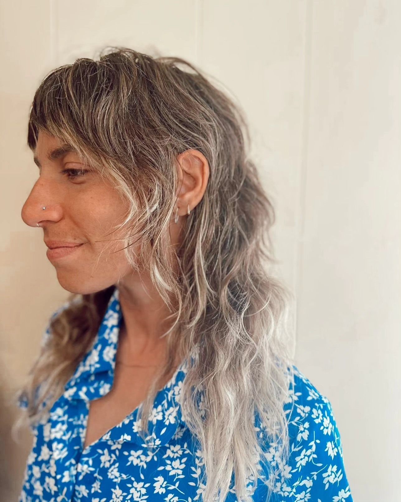 Side-profile portrait of a person with wavy gray hair wearing a blue floral shirt against a plain background