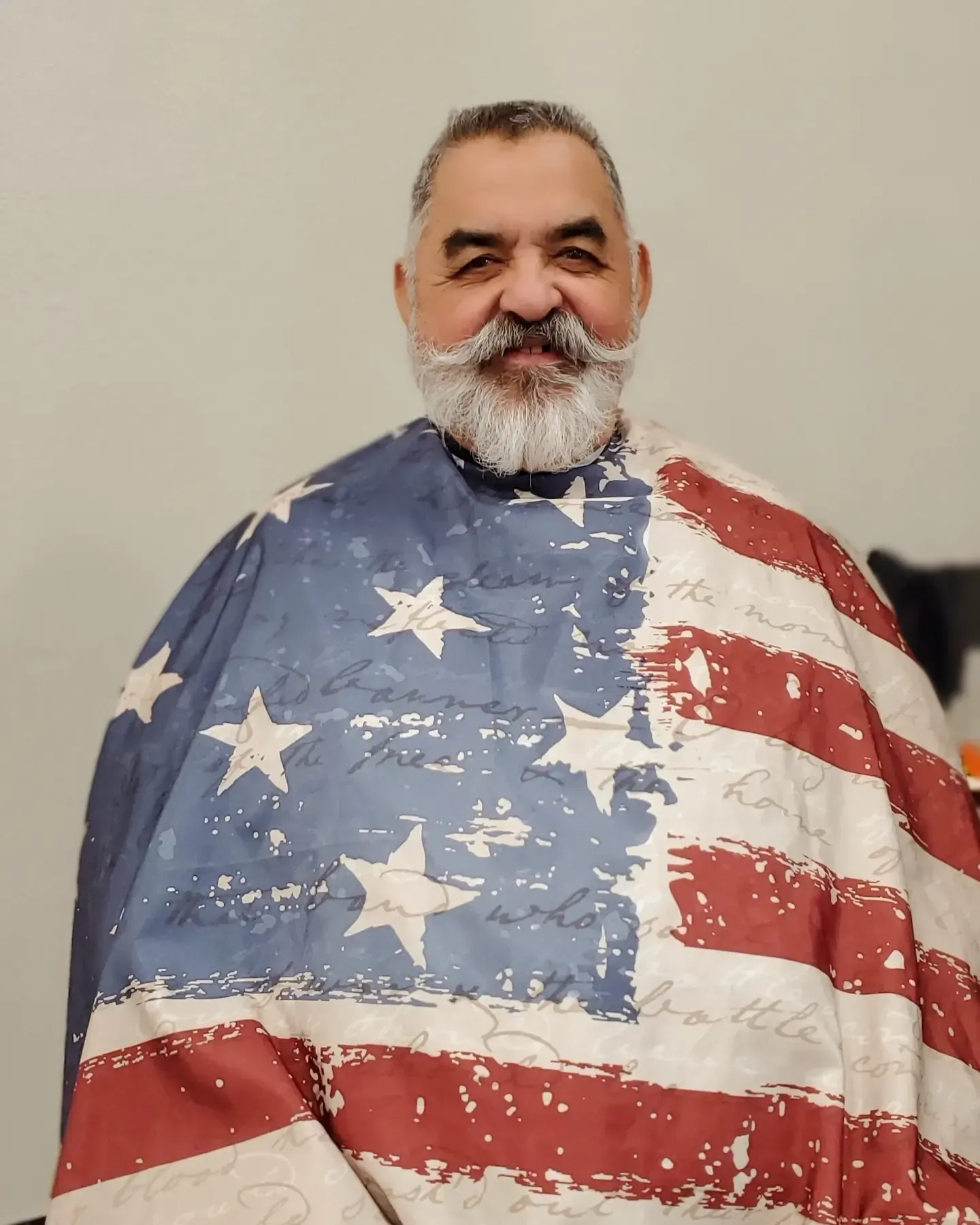Smiling man draped in a U.S. flag, standing against a plain background.