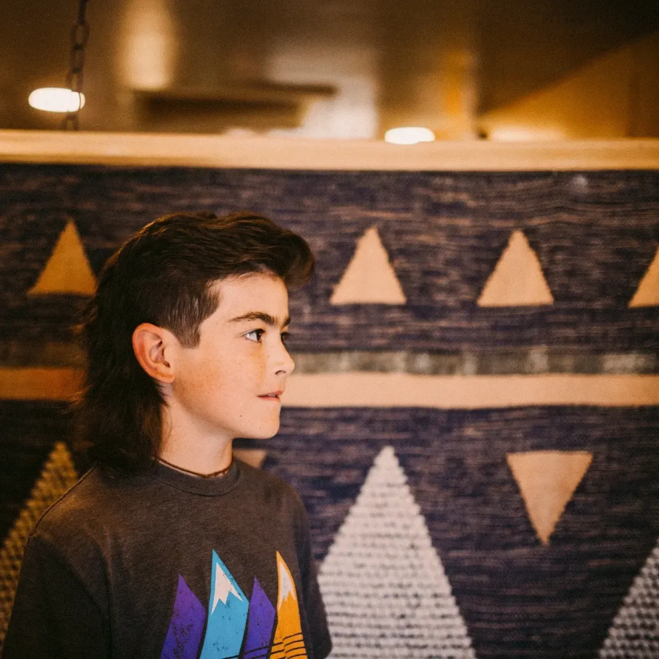 Person in profile wearing a dark shirt, standing before a patterned wall with beige triangles.