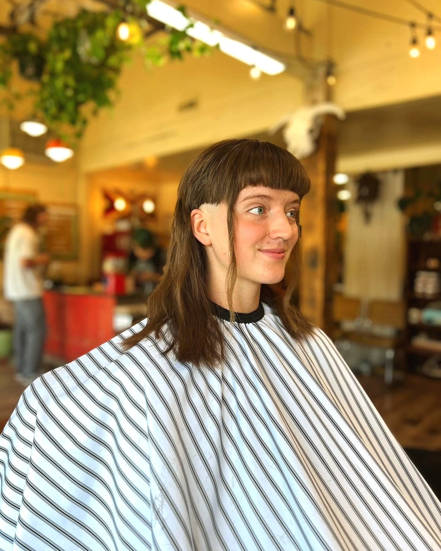 Person with long dark hair and striped cape, smiling in a bright salon chair.