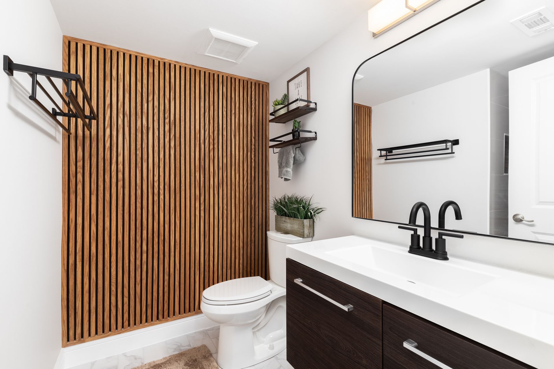 Modern bathroom with wooden accent wall, white vanity, black fixtures, and decorative shelves.