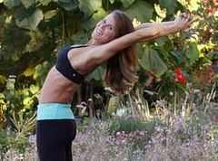 A woman is doing yoga in a garden with her arms outstretched.