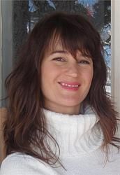 A woman with long brown hair is wearing a white sweater and smiling.