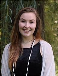 A young woman wearing a black dress and a pearl necklace is smiling for the camera.
