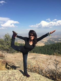 A woman is standing on one leg on top of a mountain.