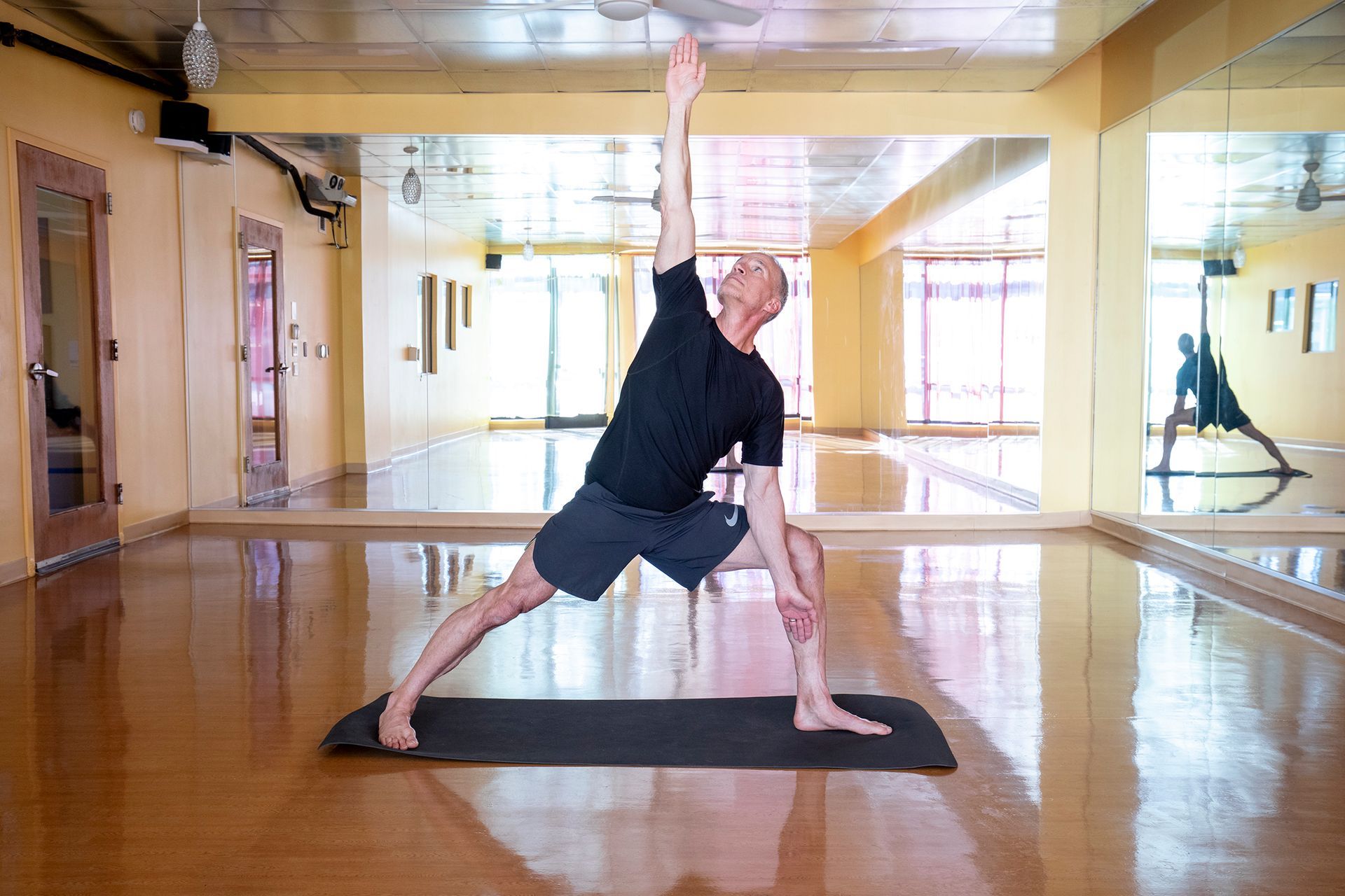 A man is standing on a yoga mat in a gym.