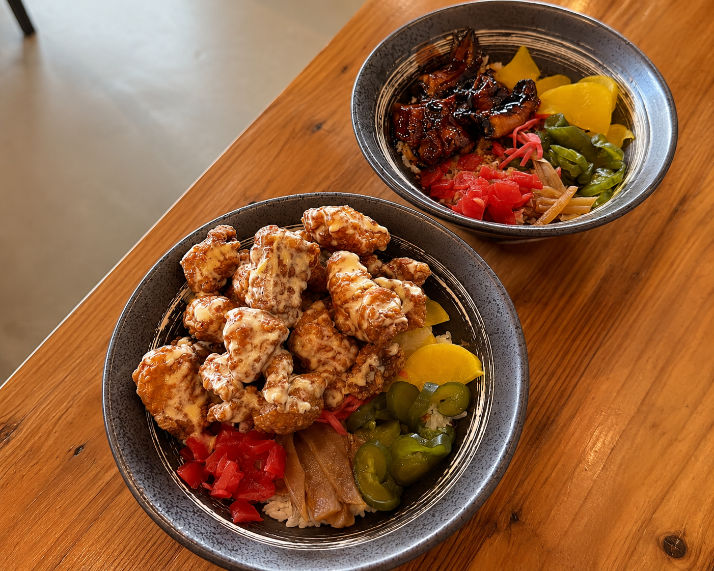 Two bowls of colorful food on a wooden table, with fried pieces and fruit toppings