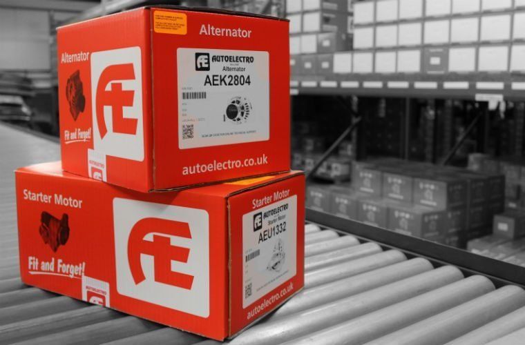 2 red boxes of Automotive parts on top of each other sat on a roller conveyor system in a warehouse with large labels on them