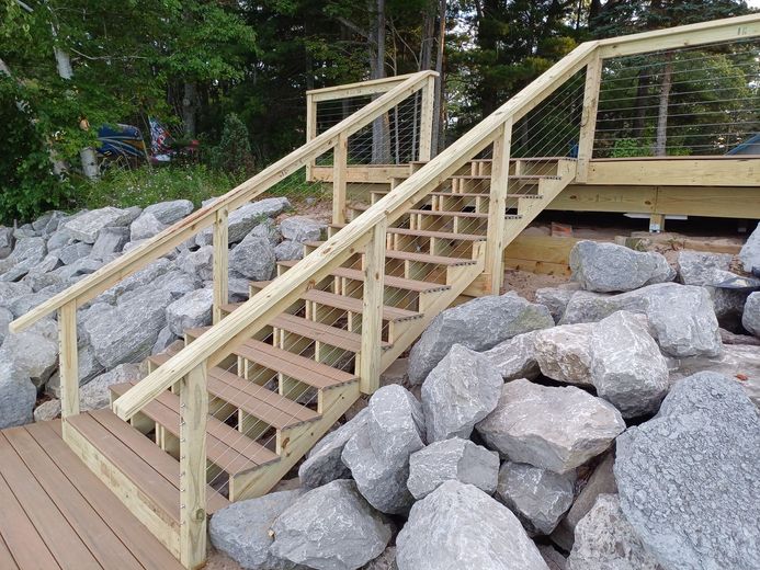 Wooden staircase with railings built over large gray rocks leading to a deck area outdoors
