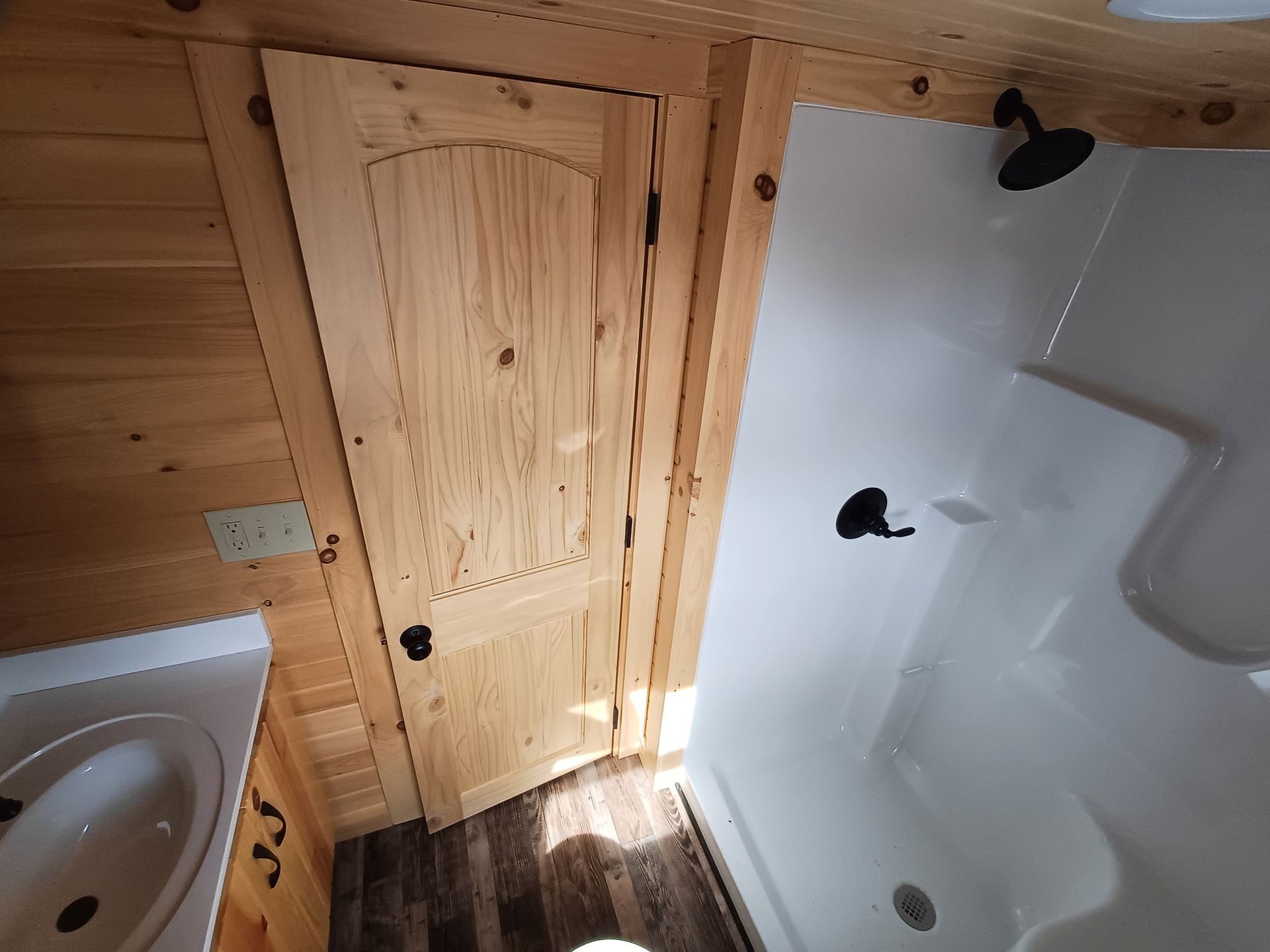 Wood-paneled bathroom with a white tub, sink, and a small wooden door by the shower.